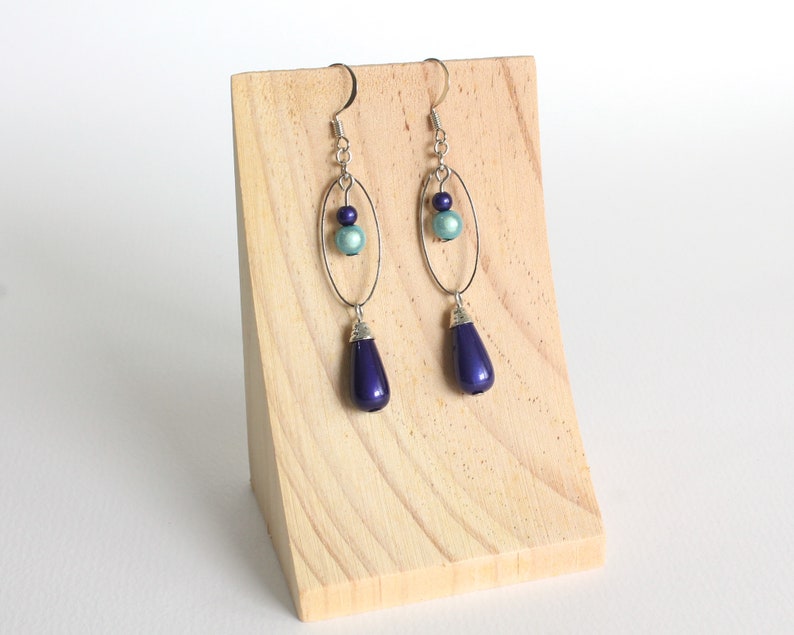 Puede incluir: Un par de pendientes colgantes con un aro ovalado plateado y una cuenta azul en forma de l&aacute;grima. Los pendientes tambi&eacute;n tienen una cuenta azul m&aacute;s peque&ntilde;a y una cuenta plateada.