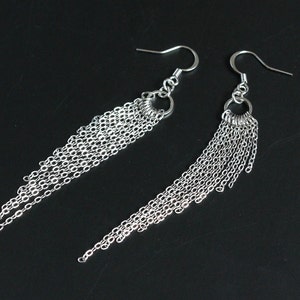 May include: A pair of silver dangle earrings with multiple chain links hanging from a small hoop. The earrings are made of metal and have a simple, elegant design.