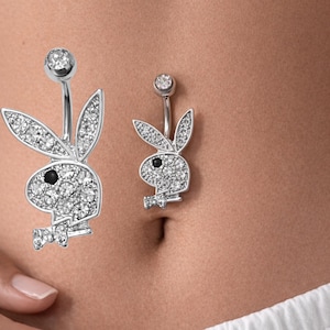 Puede incluir: Dos piercings para el ombligo plateados. Cada anillo presenta un diseño de conejito incrustado con cristales transparentes. El ojo del conejito es una piedra negra. La parte superior del anillo tiene un cristal redondo transparente.