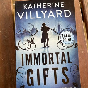 May include: Book cover for "Immortal Gifts" by Katherine Villyard. The cover features a silhouette of a person playing a violin in front of a cityscape. The book is part of the "Immortal Vampires Series" and is labeled "Large Print".