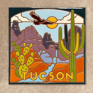 May include: Square ceramic tile featuring a desert landscape with a soaring eagle, a setting sun, and the word "TUCSON". The design includes a saguaro cactus, mountains, and a flowing river, all in vibrant colors.