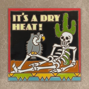 May include: A square decorative tile featuring a cartoon skeleton leaning against a green cactus with a grey vulture perched on its leg. The black background includes the text IT'S A DRY HEAT! in cream letters, framed by a red border and geometric base.