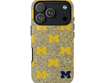 May include: A gold glitter phone case with a repeating pattern of yellow "M" logos. The case has a black camera module and black side buttons. A navy blue "M" logo is at the bottom.