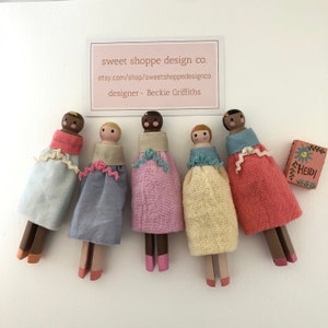 May include: Five wooden peg dolls dressed in colorful fabric dresses with a small wooden box that says "Heidi!" on it.