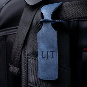 A close-up view of a black bag strap with a personalized luggage tag attached to it.