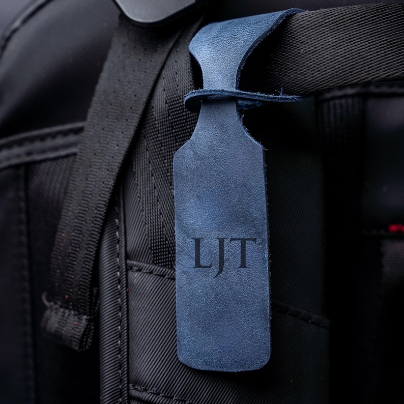 A close-up view of a black bag strap with a personalized luggage tag attached to it.