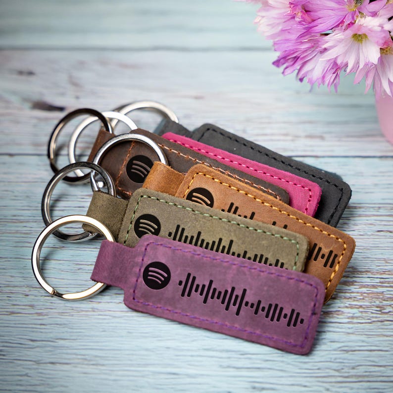 May include: A set of five leather keychains with a Spotify logo and a barcode design. The keychains are in different colors: purple, green, brown, pink, and black.
