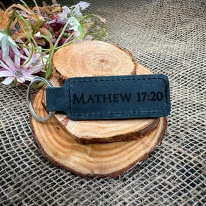 May include: Black leather keychain with a silver ring and the text "MATHEW 17:20" engraved on it.