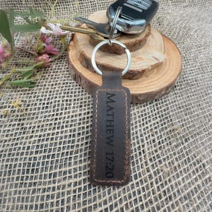 May include: Brown leather keychain with a silver ring and the text "MATHEW 17:20" engraved on the leather.