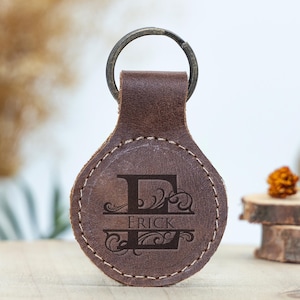May include: A brown leather keychain with a metal ring. The keychain features the letter "E" with the name "Erick" engraved in a decorative font. The leather is stitched around the edges.