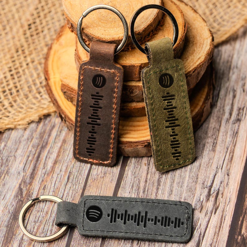 May include: Three leather keychains with a Spotify logo and a barcode design. The keychains are brown, green, and gray.