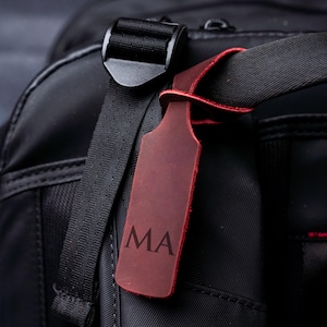 A close-up view of a black bag with a red luggage tag attached, featuring the initials 'MA'.