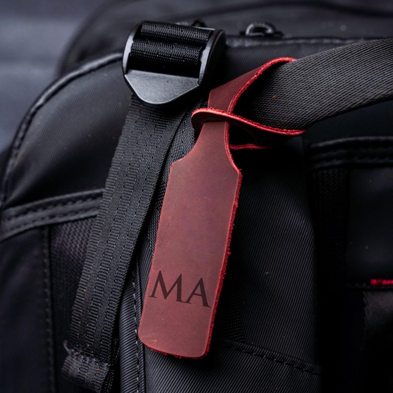 A close-up view of a black bag with a red luggage tag attached, featuring the initials 'MA'.