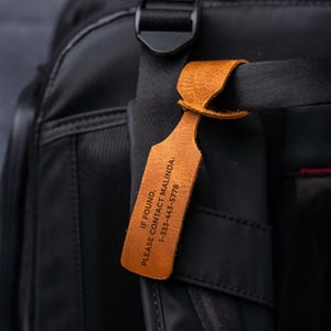 A close-up view of a black bag with a brown leather tag attached, displaying contact information.