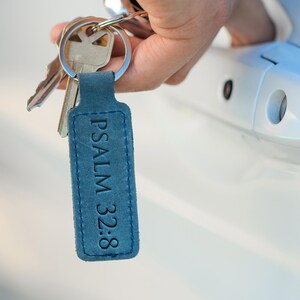 May include: A blue leather keychain with the text "PSALM 32:8" in black lettering. The keychain is attached to a set of keys.