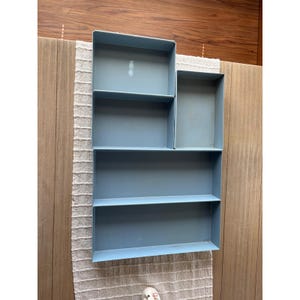 May include: A light blue metal drawer organizer with five rectangular compartments of varying sizes. The organizer features a smooth finish and clean, straight edges, designed with an open-top structure for storage and organization.