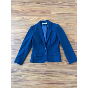 May include: A white ceramic mug with a black handle and the text "But First, Coffee" in a black, handwritten-style font. The mug is on a white surface.