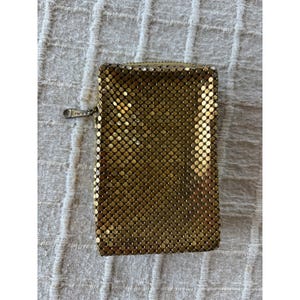 May include: A rectangular gold-toned metal mesh pouch featuring a fine chainmail texture. The accessory includes a top zipper closure with a small metal pull tab. The surface is composed of numerous tiny, interconnected circular metal plates.