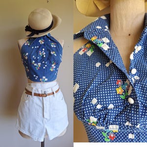 May include: A blue halter top with a white polka dot pattern and small floral clusters, featuring a pointed collar and white buttons. The top is paired with white denim shorts and a thin brown leather belt. A beige hat with a black ribbon is included.