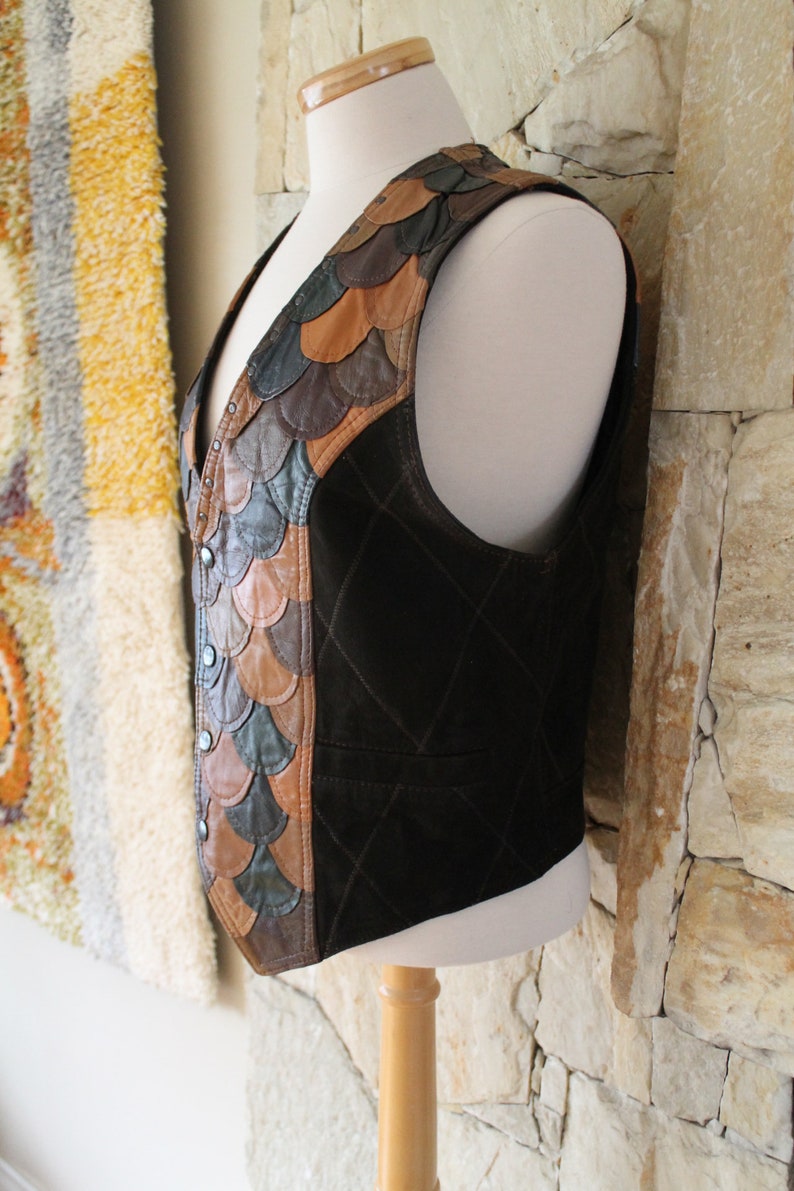 May include: A brown leather waistcoat with a quilted design and a decorative panel of brown, tan, and green leather scales on the left side.