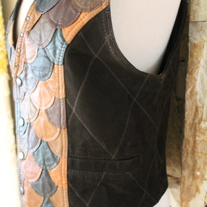 May include: A brown leather waistcoat with a quilted design on the back and a patchwork of different coloured leather on the front. The waistcoat has a V-neck and a button closure.