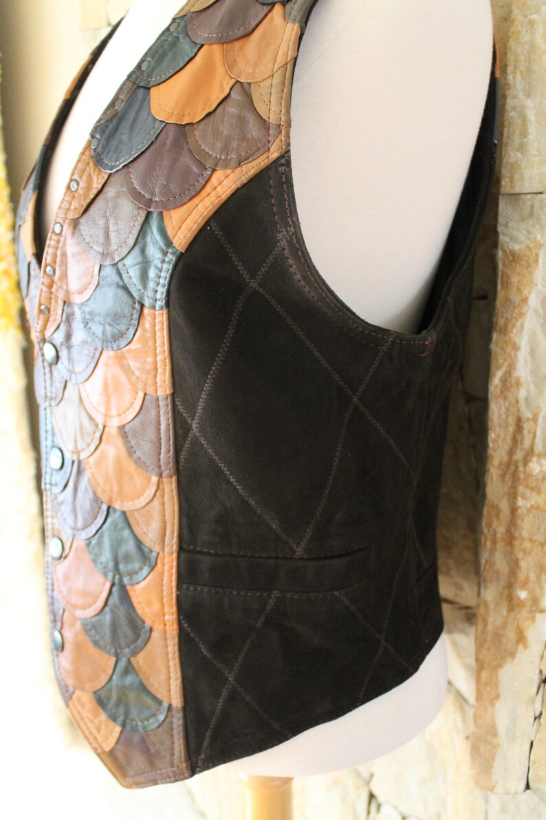 May include: A brown leather waistcoat with a quilted design on the back and a patchwork of different coloured leather on the front. The waistcoat has a V-neck and a button closure.