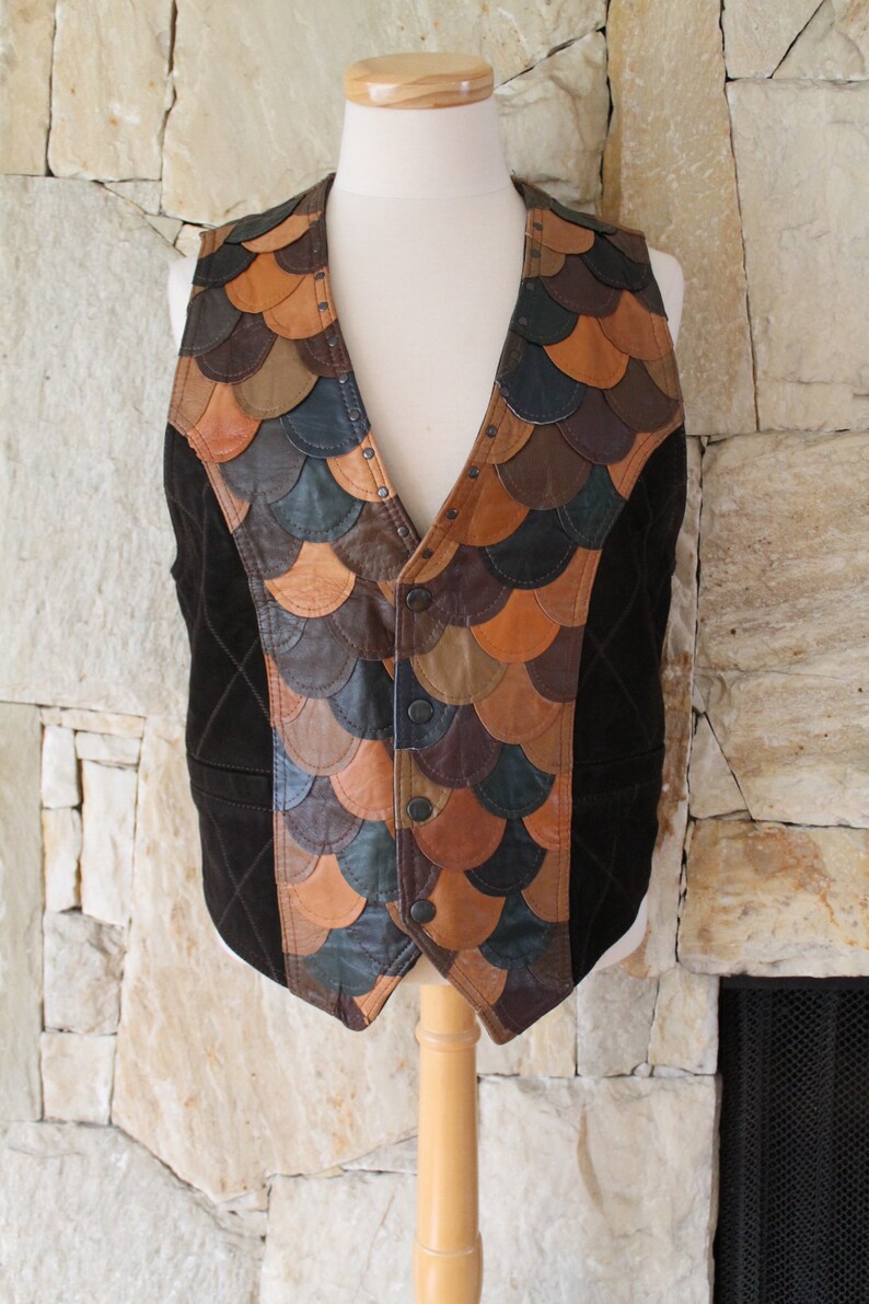 May include: A brown leather waistcoat with a unique design featuring a patchwork of different coloured leather pieces. The waistcoat has a V-neck and a button closure.