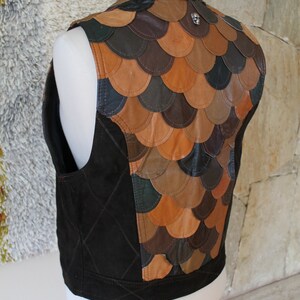 May include: A brown leather waistcoat with a quilted front and a back made of overlapping leather scales. The waistcoat has a small silver skull charm on the back.