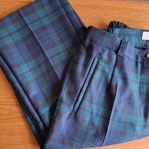 May include: A pair of folded plaid pants in shades of blue and teal. The pants have a button and a zipper closure, with pleats at the front. The fabric appears to be a woven material.