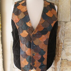 May include: A brown suede waistcoat with a unique design featuring a patchwork of leather scales in shades of brown, tan, and black. The waistcoat has a button closure and is accented with metal studs.