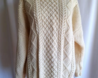 May include: A cream-coloured cable knit jumper with a classic crew neck. The jumper is made of a soft, warm material and features a traditional Irish cable knit pattern.