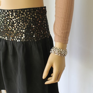 May include: A black skirt with a gold sequin waistband. The skirt is made of a soft, flowing fabric and has a simple, elegant design.