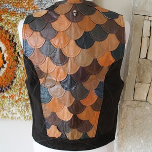 May include: A brown leather waistcoat with a unique design featuring a pattern of overlapping leather scales. The waistcoat has a skull-shaped button on the back.
