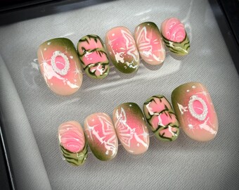 May include: A set of press-on nails with a pink, green, and white design. The nails feature a variety of patterns, including floral and geometric designs, and some have a sparkling embellishment. The nails are oval-shaped and are arranged in two rows.