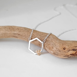 May include: A silver necklace with a hexagonal pendant featuring a gold bee. The pendant is open and the bee is inside the hexagon.