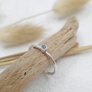 May include: A silver ring with a small, light blue gemstone set in the centre.