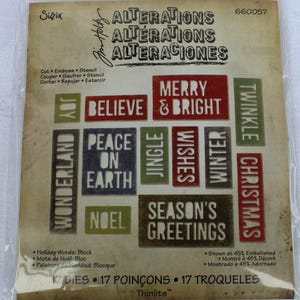 May include: A package of 17 metal dies for crafting. The dies feature Christmas-themed words and phrases, including "Merry & Bright", "Peace on Earth", "Jingle Wishes", and "Season's Greetings". The package is labeled "Sizzix Thinlits" and includes instructions in English, French, Spanish, and German.
