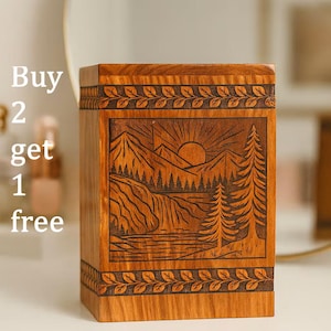 May include: A wooden box with a carved landscape scene featuring mountains, a waterfall, and trees. The box has a rectangular shape with leaf-patterned borders. The wood has a warm, natural tone.