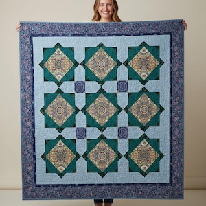 Puede incluir: Un edredón grande y cuadrado con un fondo azul claro y un borde floral azul oscuro. El edredón presenta un patrón repetitivo de diamantes turquesa con diseños circulares ornamentados en el centro. El edredón se sostiene, mostrando su tamaño y detalles intrincados.