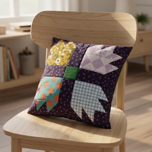 May include: Square patchwork cushion with a dark purple background and various fabric squares. The squares feature floral, polka dot, and gingham patterns in yellow, orange, and blue. The cushion is placed on a wooden chair.