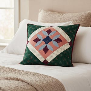 Puede incluir: Cojín decorativo cuadrado con diseño de patchwork. El cojín presenta un fondo verde con un patrón de diamantes, un cuadrado central con un diseño floral en rosa, azul y burdeos, y un borde rojo.