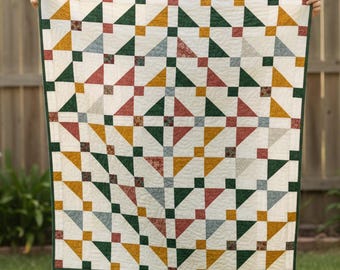 Pode incluir: Um edredom feito à mão com um padrão geométrico. O edredom apresenta triângulos e quadrados em tons de verde, dourado, vermelho e cinza sobre um fundo creme. O edredom é adornado com uma borda verde.