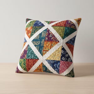 Peut inclure: Coussin carré décoratif avec un motif patchwork. Le coussin présente une variété de carrés de tissu colorés dans les tons de rouge, vert, bleu, jaune et violet, disposés en motif géométrique. Des bandes de tissu blanc forment une grille sur le patchwork.