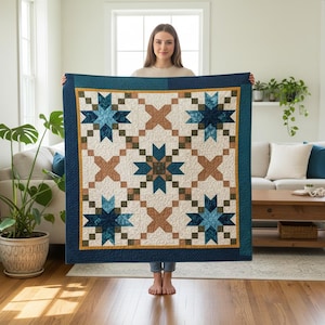 May include: A handmade quilt featuring a starburst pattern in shades of blue, brown, and cream. The quilt has a dark blue border with a gold accent. The design is symmetrical and geometric, suitable for a bed or wall hanging.
