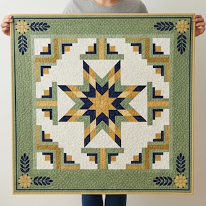 May include: A square quilt featuring a central star pattern in gold and navy blue, on a white backdrop. The quilt is bordered by a green frame with floral and leaf patterns. The design is geometric and symmetrical, with a traditional aesthetic.