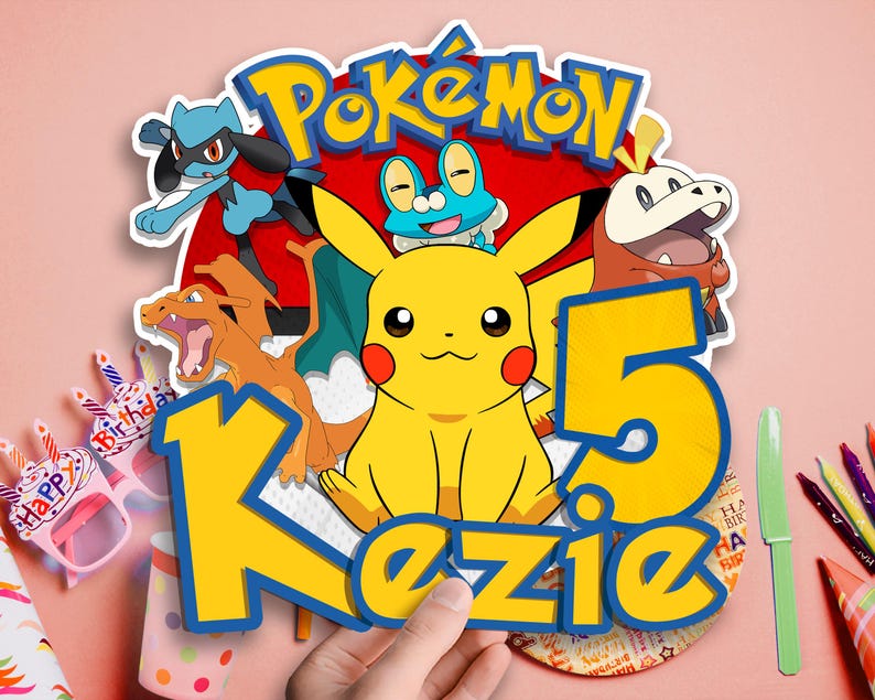 May include: A colorful Pok&eacute;mon-themed birthday cake topper featuring Pikachu, other characters, and the name "Kezie" with the number "5". The design includes a red background with the Pok&eacute;mon logo and various cartoon characters.