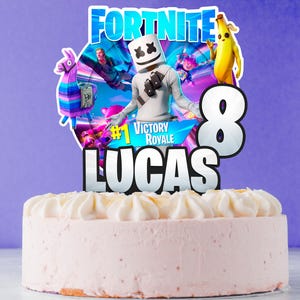 May include: A pink frosted cake with a decorative topper featuring the word "Fortnite", the number "8", and the name "Lucas". The topper includes cartoon characters and the words "Victory Royale".