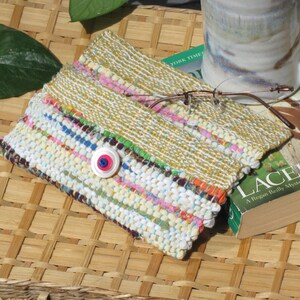 Boho Wallet Smart Phone Case, Small Hand Woven Clutch Purse, Cloth Fabric Soft Eyeglass Case Handmade Vegan Eco Friendly Zero Waste Upcycled Recycled Bag, Sustainable Slow Fashion Accessory with Sunny Yellow Accents Handcrafted by Amy C. Lund! Showing button closure. Styled open with reading glasses, a mug and a book on a basket with green leaves.