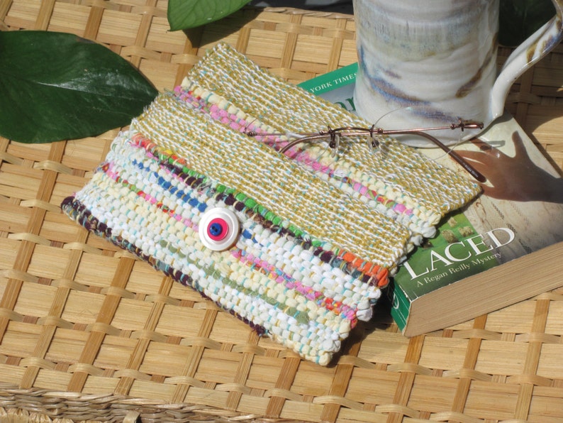 Boho Wallet Smart Phone Case, Small Hand Woven Clutch Purse, Cloth Fabric Soft Eyeglass Case Handmade Vegan Eco Friendly Zero Waste Upcycled Recycled Bag, Sustainable Slow Fashion Accessory with Sunny Yellow Accents Handcrafted by Amy C. Lund! Showing button closure. Styled open with reading glasses, a mug and a book on a basket with green leaves.