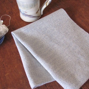 A white and light blue Twill Block patterned hand woven towel, shown as an example for Table or Floor Loom Weaving Pattern Draft PDF, 4 H Harness Shaft Handweaving Cotton Kitchen Hand Woven Dish Tea Towel Downloadable Tutorial, an artful Kitchenware, Cookware Accessory for Gourmet Chef, Home Baking, Cooking, Instructions Designed by Master Weaver Amy C. Lund. Pictured with  a ceramic mug and tea bag.